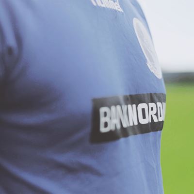 En fodboldspiller står på banen i sin trøje, der er sponsoreret af BankNordik