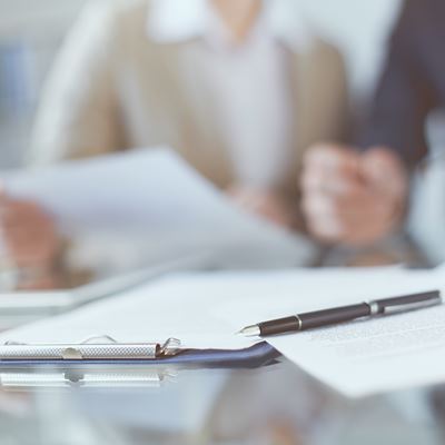 Et clipboard og en kuglepen ligger på et bord hvor en mand og en kvinde gennemgår nogle papirer