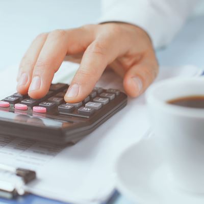 En mand taster på en lommeregner, der ligger på en bord med et clipboard og en kop kaffe