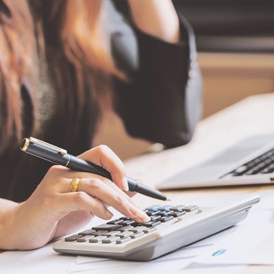 En kvinde sidder ved et skrivebord med sin computer og taster på en lommeregner