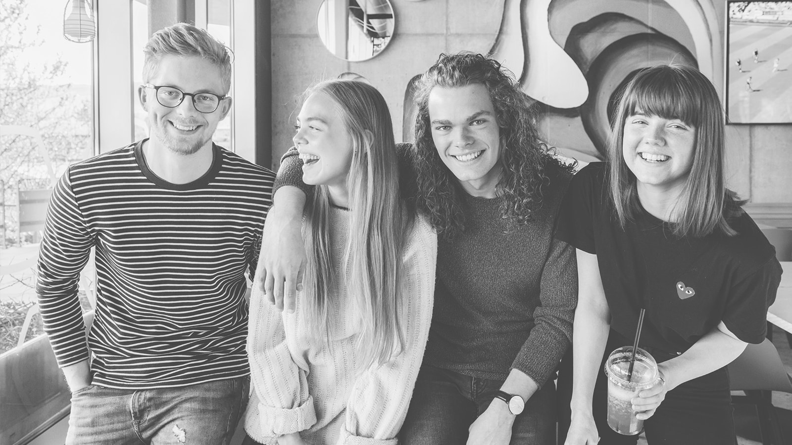 En gruppe unge sider sammen på en café og smiler