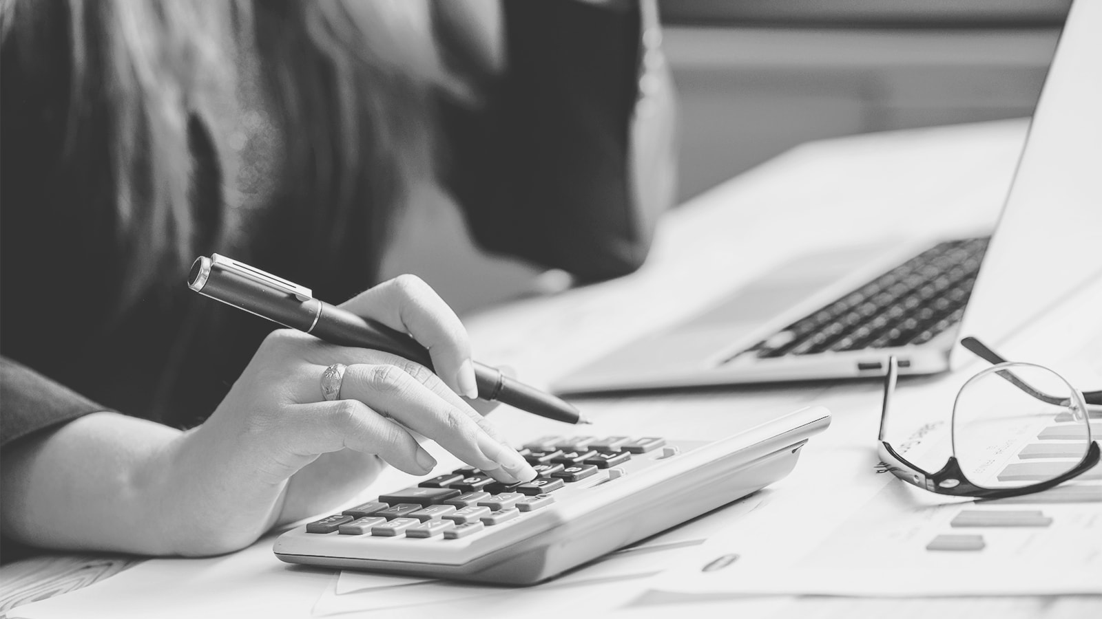 En kvinde sidder ved et skrivebord med sin computer og taster på en lommeregner