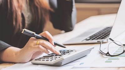 En kvinde sidder ved et skrivebord med sin computer og taster på en lommeregner