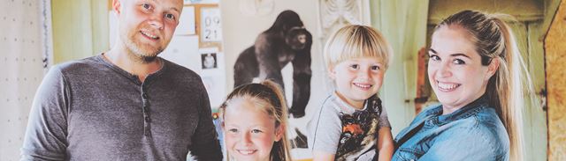 En familie med mor, far og to børn kigger glad ind i kameraet