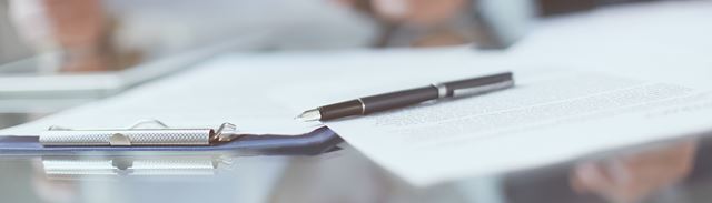 Et clipboard og en kuglepen ligger på et bord hvor en mand og en kvinde gennemgår nogle papirer