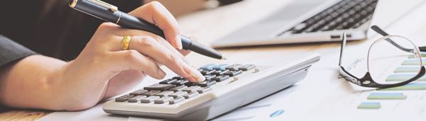 En kvinde sidder ved et skrivebord med sin computer og taster på en lommeregner