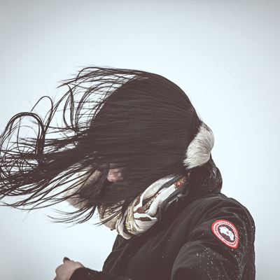 En pige er ude i blæsevejr og får vind i håret så det dækker hele hendes ansigt.