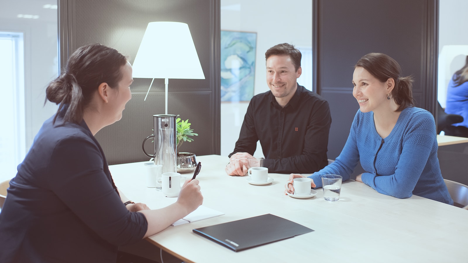 To kunder sidder ved siden af hinanden og snakker med en kunderådgiver på den anden side af bordet. 