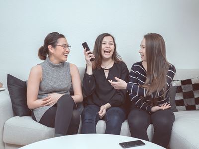 Tre teenagere sidder på en sofa med en fjernbetjening. 