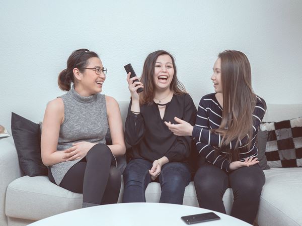 Tre teenagere sidder på en sofa med en fjernbetjening.