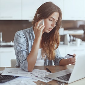 En kvinde sidder med sin computer og snakker telefon. 
